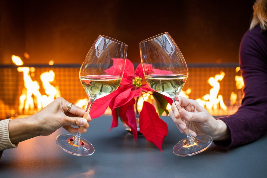 Two people clinking wine glasses in front of the fire